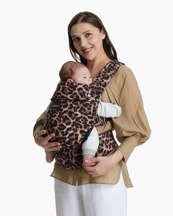 Woman in beige holding baby in leopard print Momcozy ergonomic baby carrier.