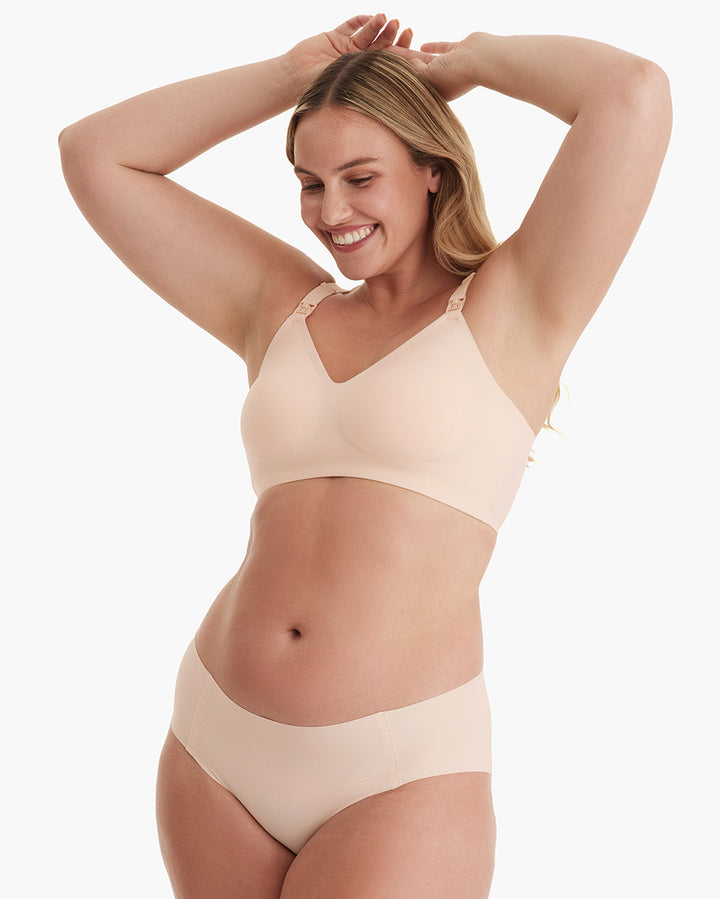 Smiling model in light peach YN21 Ultra Soft Seamless Nursing Bra. Features V-neck, streamlined comfort, and M5 pump clips.